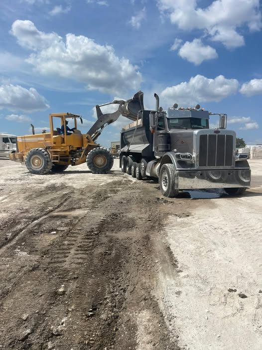 A loader filling a chrome multi-axle dump truck at a material yard.