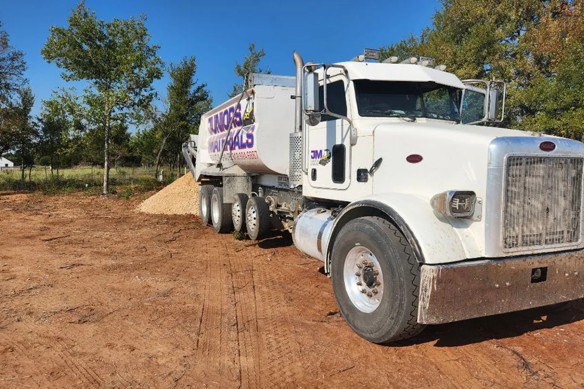 Juniors Materials dump truck parked beside a pile of delivered aggregate on a cleared lot