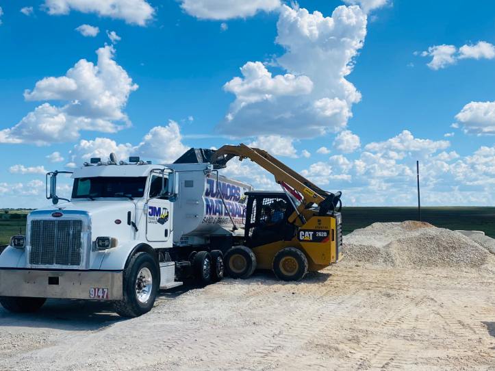 A Juniors Materials dump truck and CAT loader beside stockpiled aggregate.