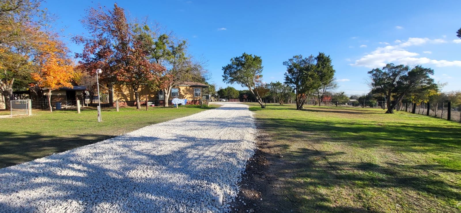 A finished gravel driveway running through a lawn with fall trees.