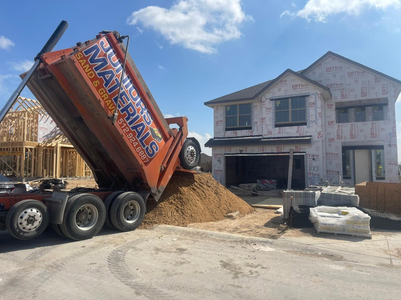 An orange Juniors Materials truck dumping at a framed two-story home.